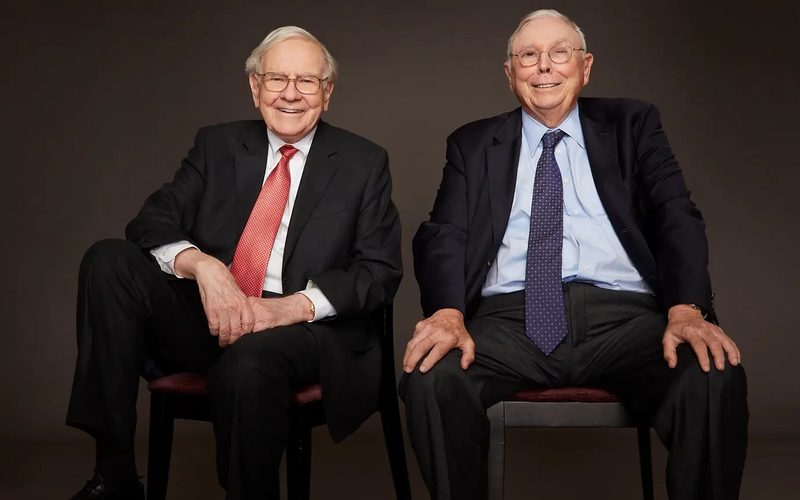 Ảnh chân dung studio: Buffett cà vạt đỏ, Munger cà vạt xanh, cùng ngồi và cười