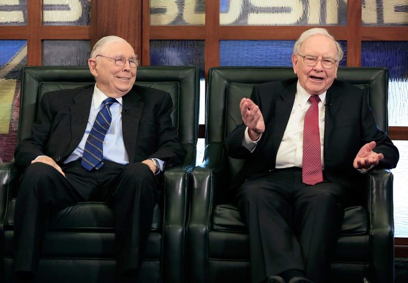 Munger và Buffett ngồi hai ghế da xanh, Buffett vung hai tay khi giải thích